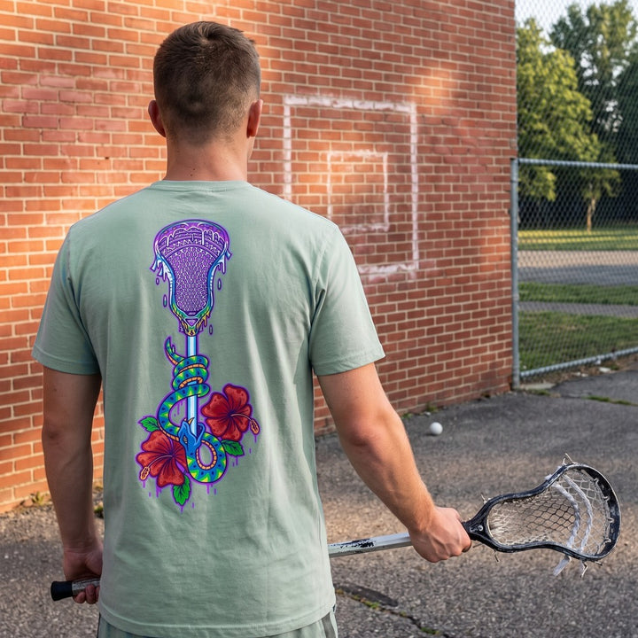 Lax Snake Tee in seafoam at a brick wall-ball court, back view showing the lacrosse stick, snake and hibiscus print